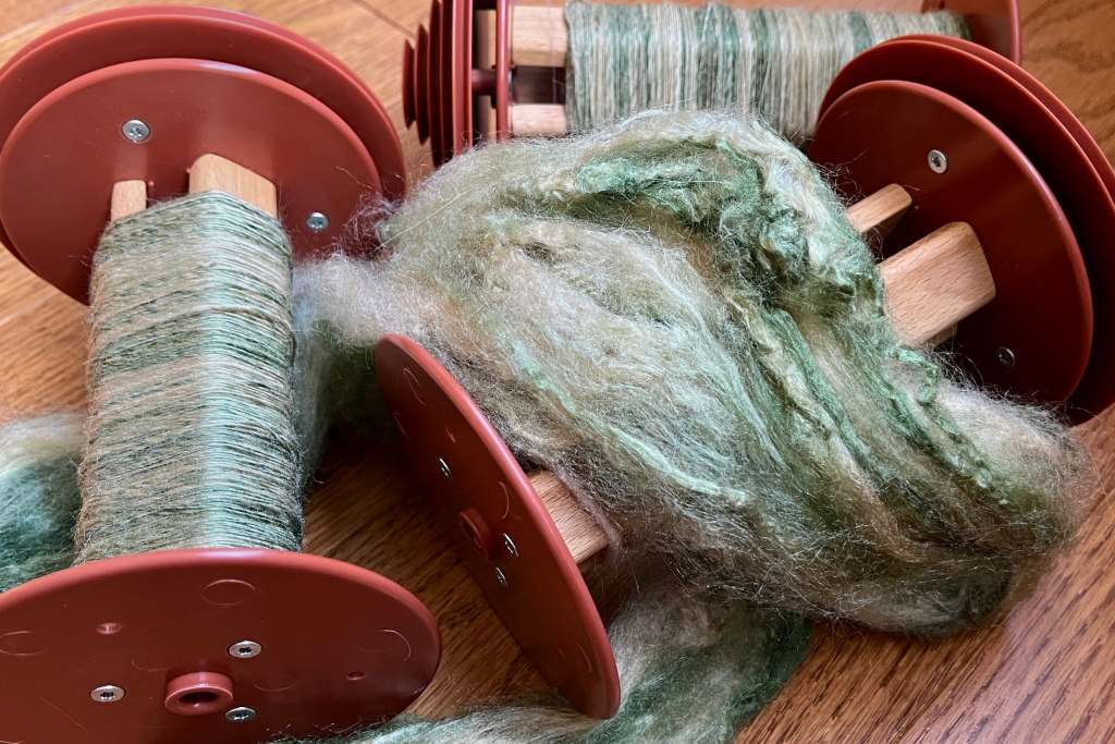 Thee Lojan bobbins, two with singles of green variegated silk, the other draped with silk unspun.